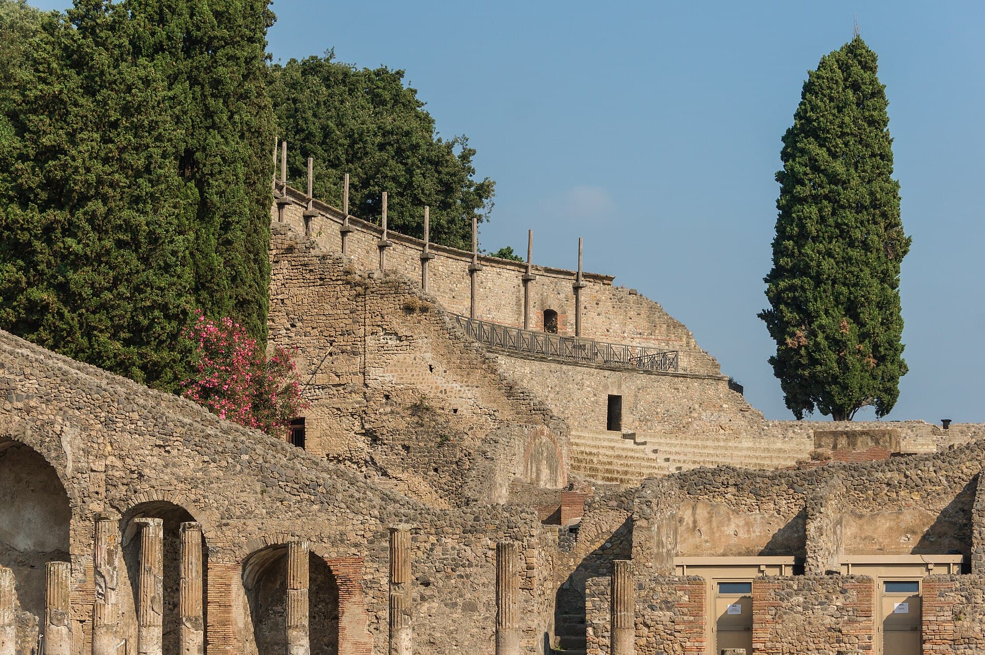 The Odeon at Pompeii, seen across ruined walls, with a curved seating bank and cypress trees.